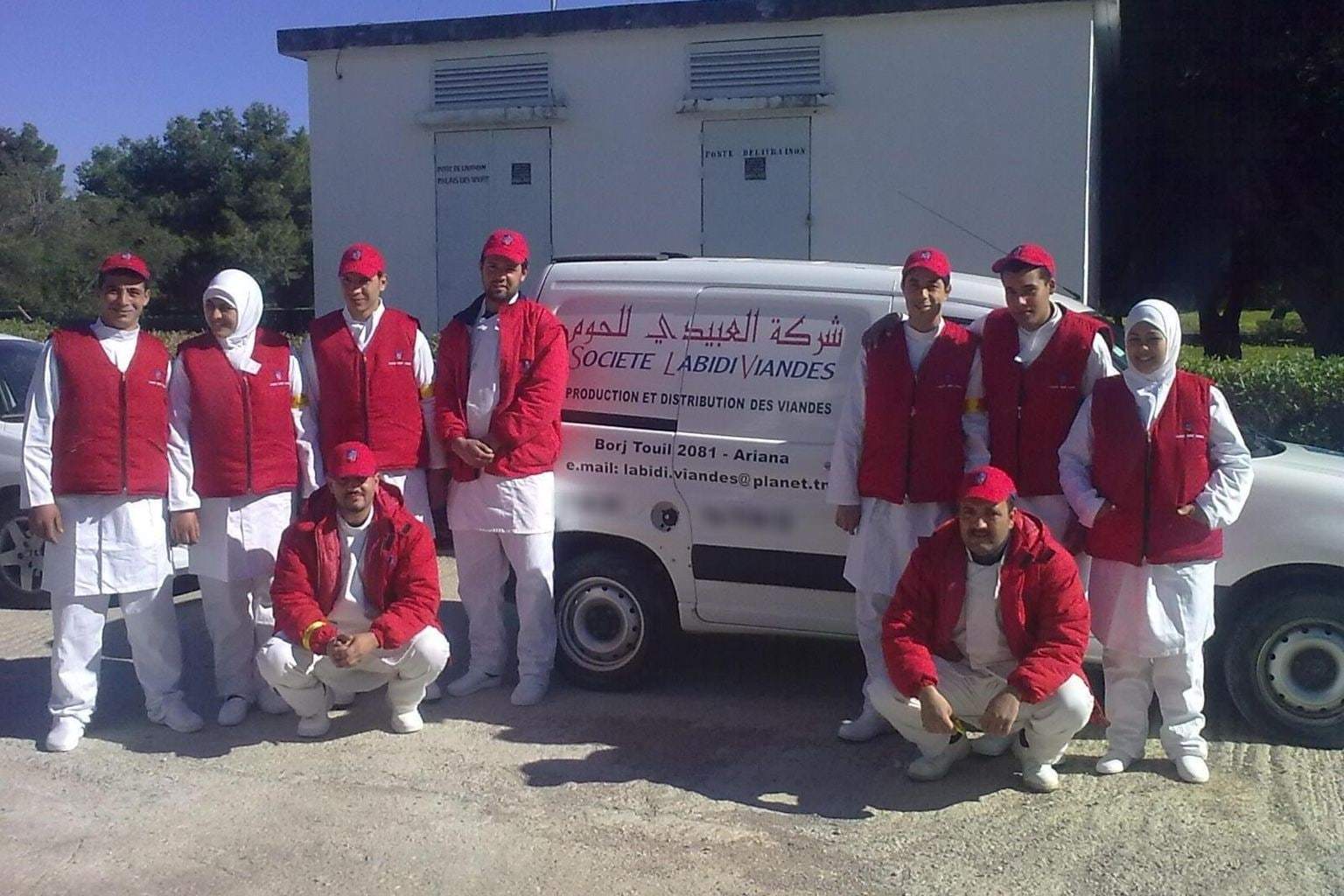 أول فريق عمل ميداني لشركة العبيدي للحوم بزيّ أحمر أمام مركبة توزيع