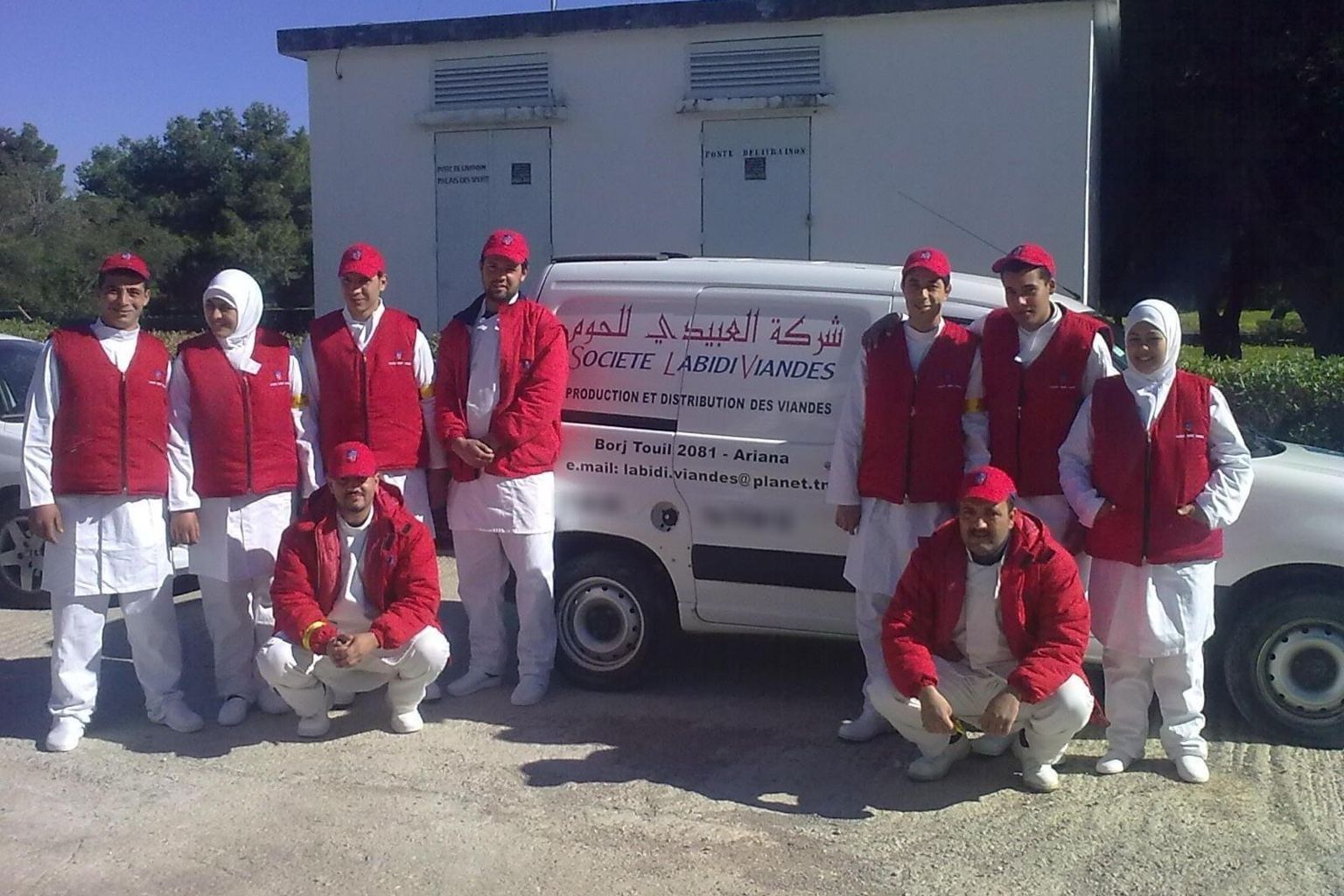 فريق شركة العبيدي للحوم بالزيّ الأحمر أمام إحدى مركبات التوزيع التابعة للشركة
